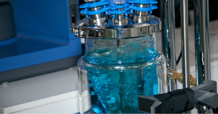 Close-up de um reator de vidro em operação, mostrando o fluxo de líquidos durante a produção de fármacos.